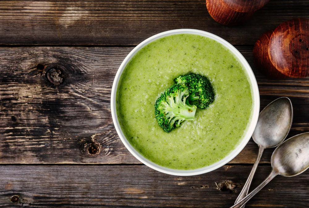 broccoli soup with whole broccoli garnish in a white bowl on a wooden table