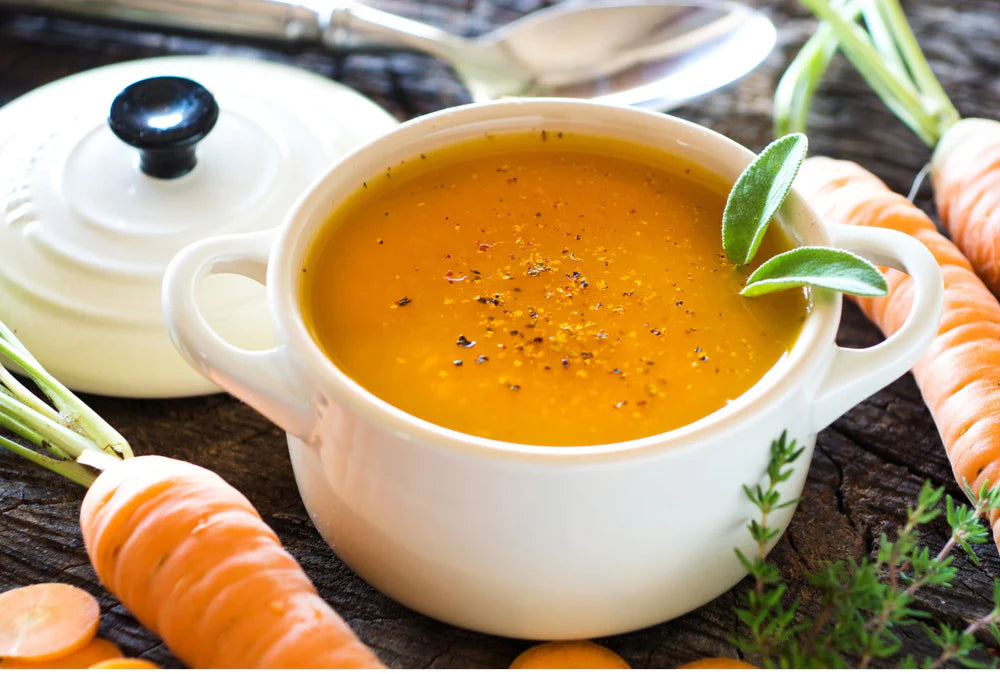 carrot soup in a white dutch oven with the lid off surrounded by fresh ingredients