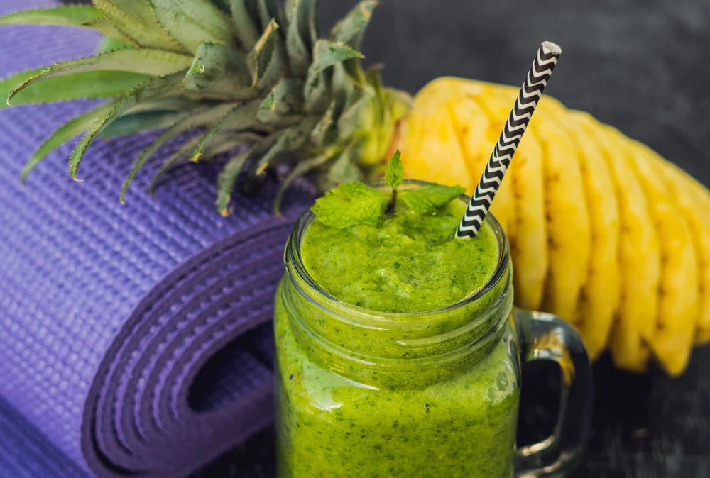 kale pineapple smoothie in a mason jar with garnish and a straw, pineapple and yoga mat in background