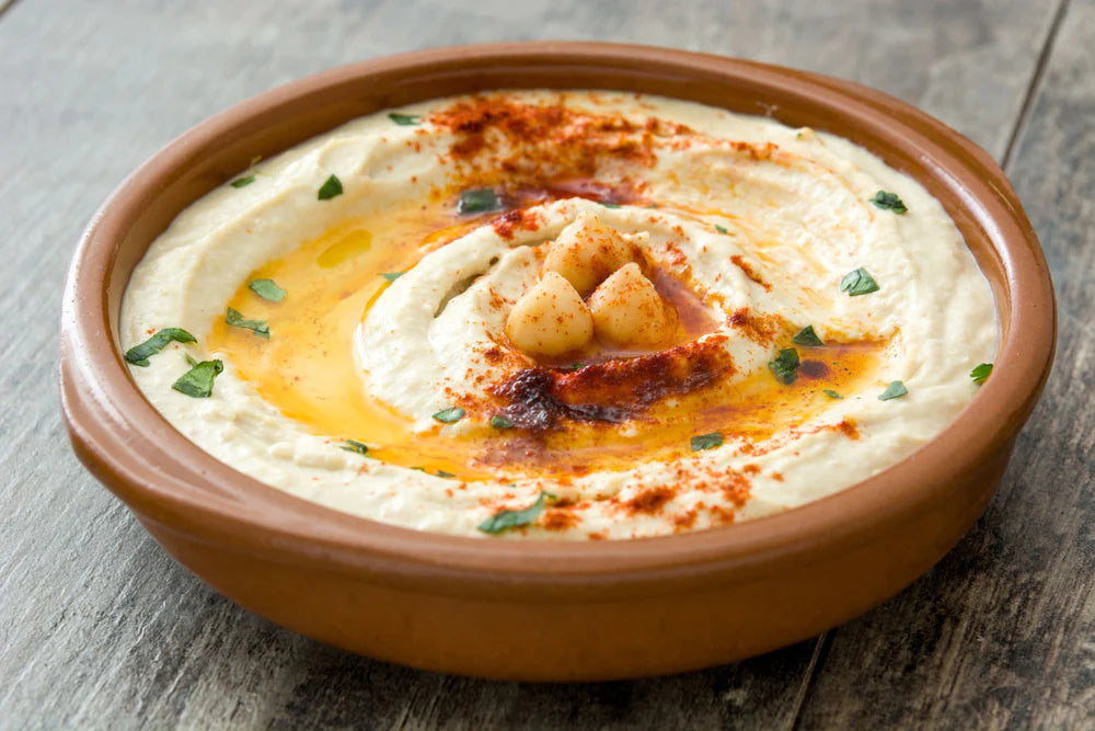 hummus with chickpea and paprika garnish in a serving dish on a wooden table