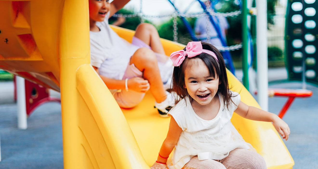 Children on a playground going down a yellow slide