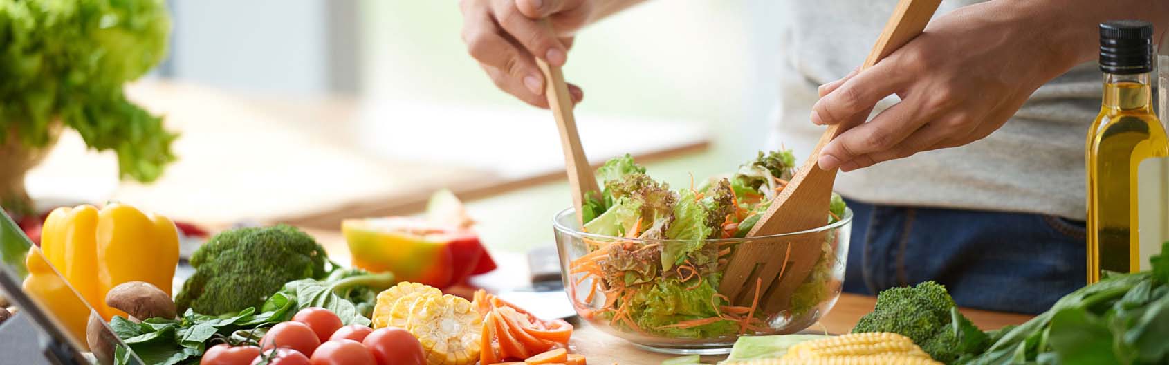 Man preparing a vegan salad in the kitchen with lettuce, mushrooms, onions, and corn