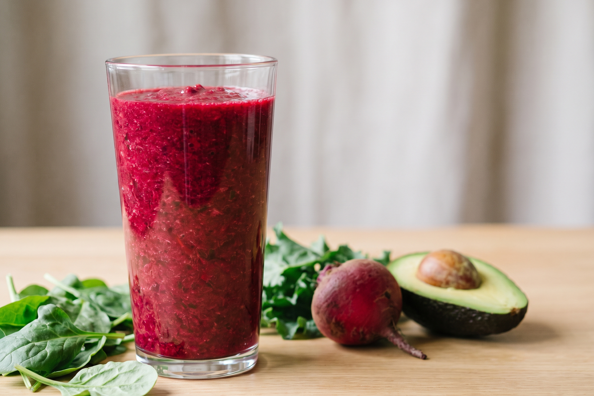 Glass of magenta beet and kale vegetable smoothie with fresh beet and kale