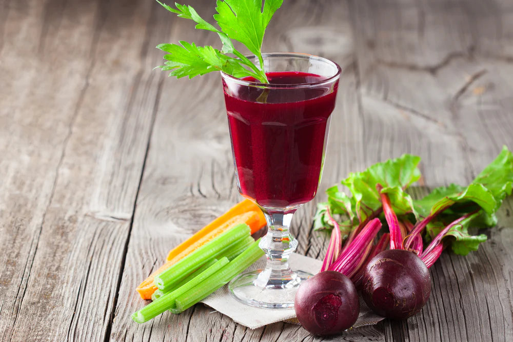 healthy vegetable juice in a glass goblet with beets, carrots, and celery on a wooden surface