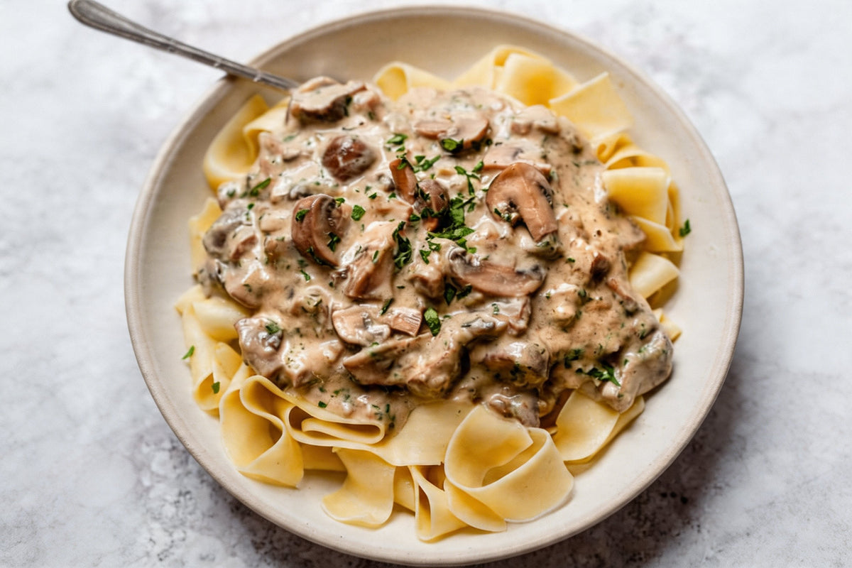 Creamy mushroom stroganoff over wide noodles in a shallow bowl, finished with chopped parsley.