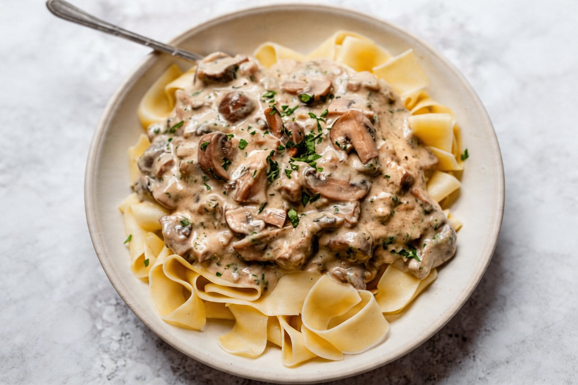 Creamy mushroom stroganoff over wide noodles in a shallow bowl, finished with chopped parsley.