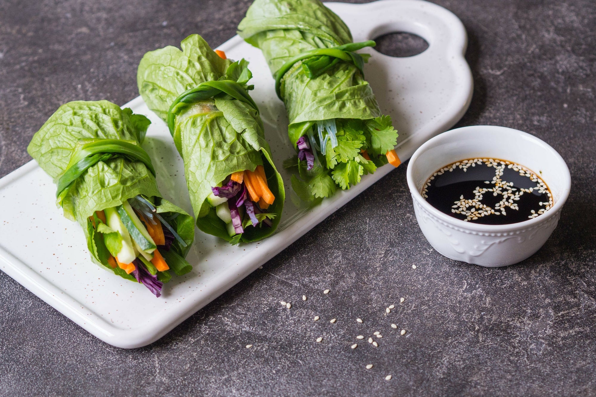 Raw veggie wraps rolled in leafy greens with a small bowl of dipping sauce