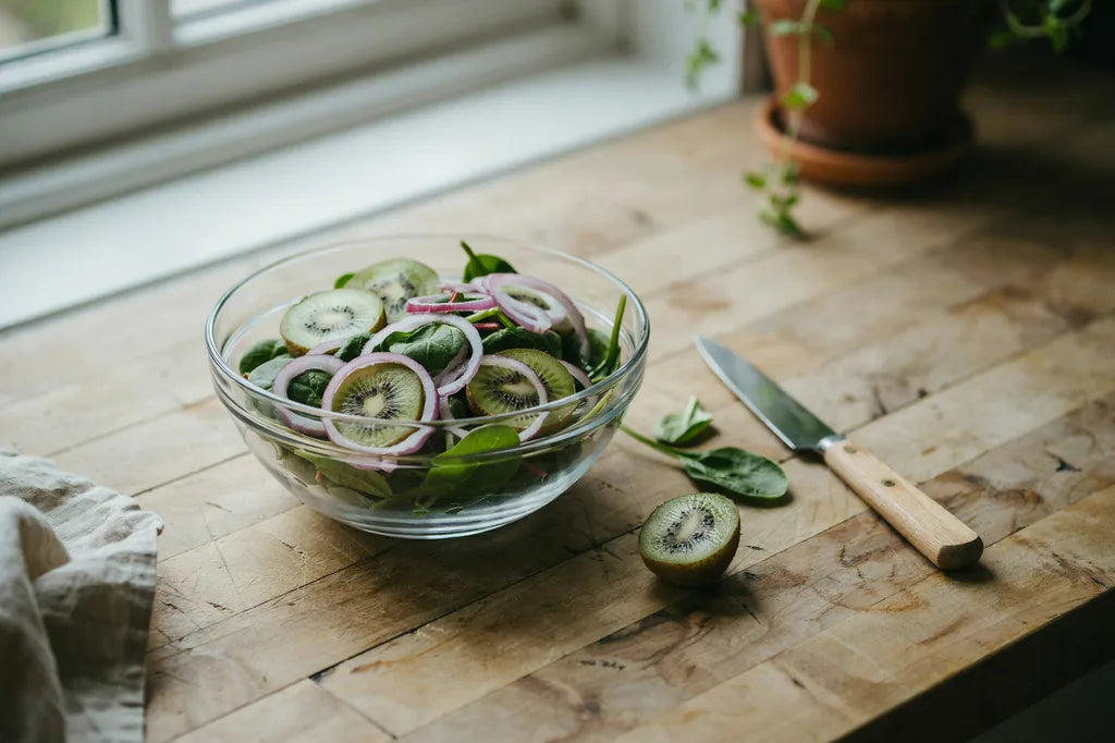 Spinach Kiwi Salad - a glass bowl of fresh spinach with sliced kiwi and purple onion