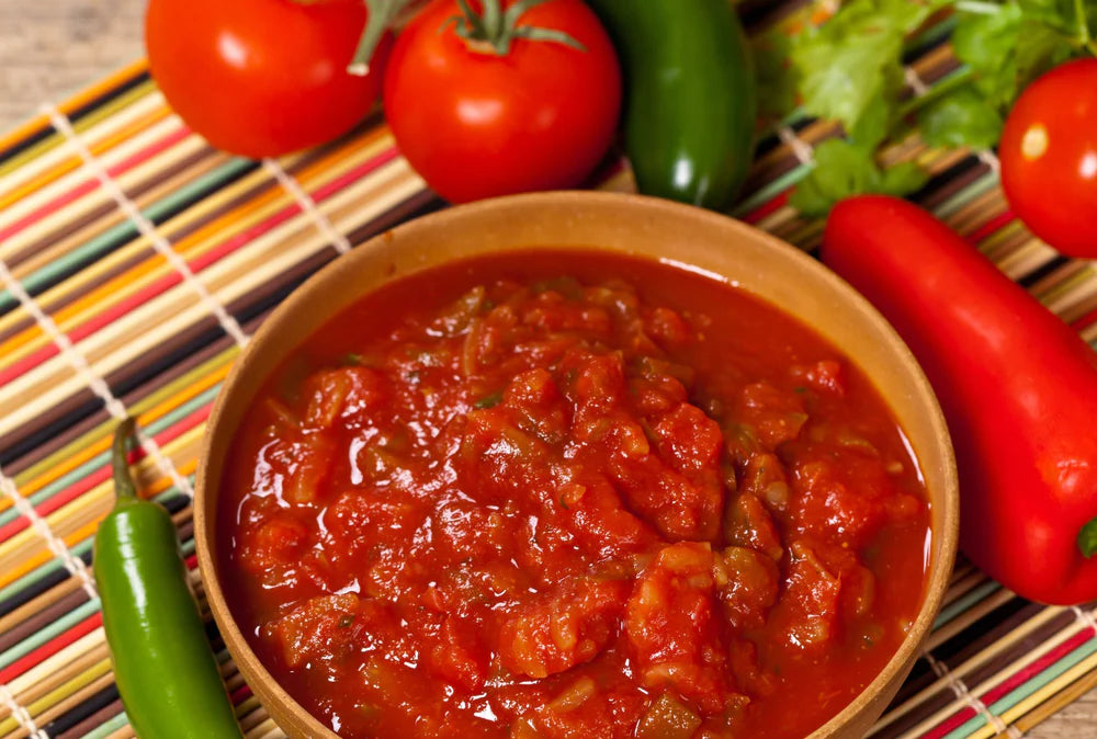 tomato salsa in a small serving bowl with fresh peppers and tomatoes surrounding