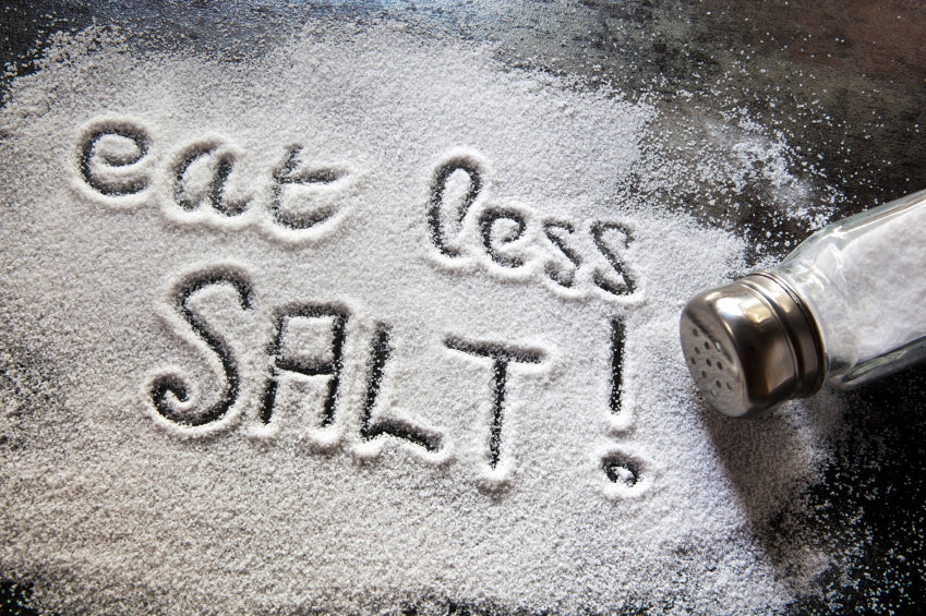 eat less SALT! written in a pile of spilled salt on a countertop with a salt shaker
