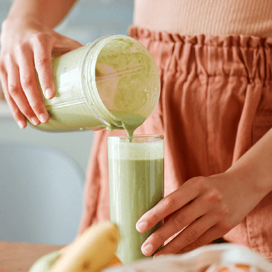 Pouring a green detox smoothie into a glass
