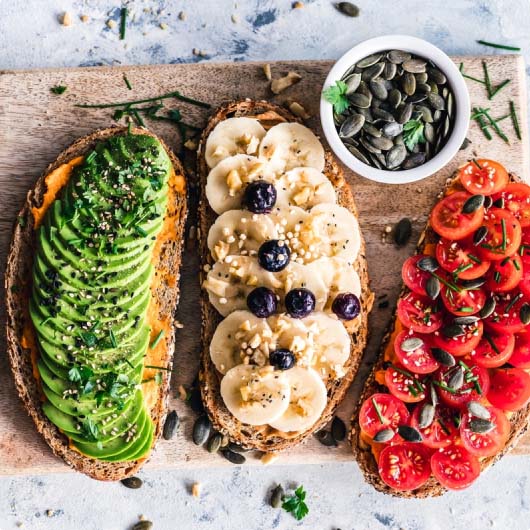 Raw vegan snacks with toast topped with avocado, bananas, tomatoes, and pepita seeds